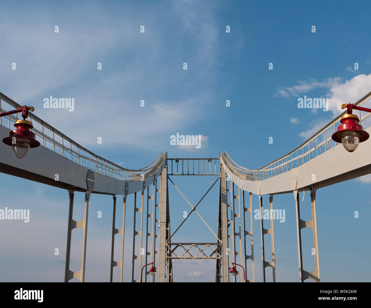 Ponte di ferro rosso con città moderne lanterne. prospettiva profonda, colonne ponte conduce al cielo blu su sfondo. Foto Stock