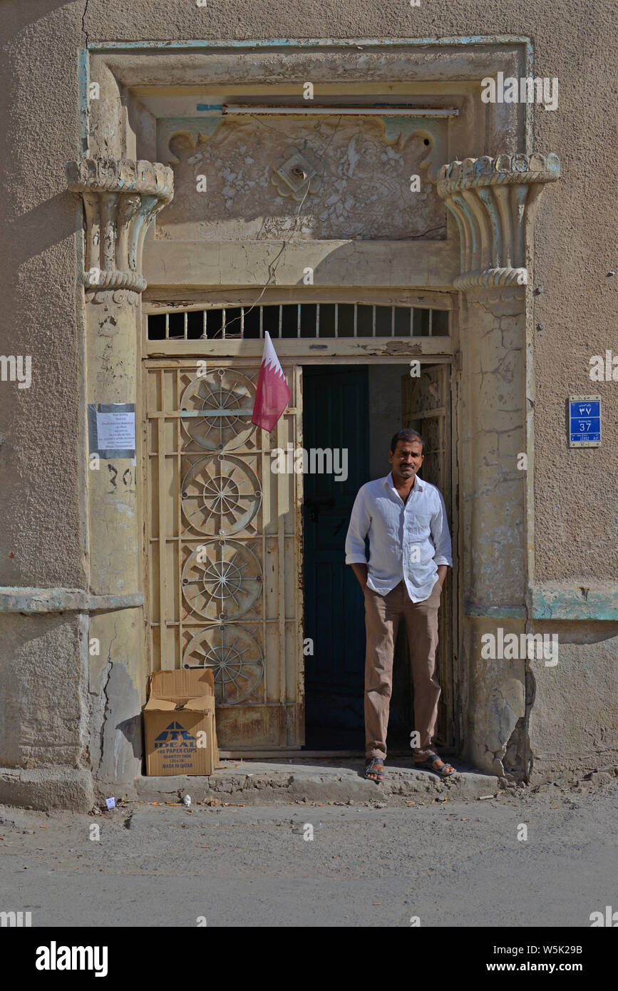 DOHA, Qatar - 25 Marzo 2016: Un indiano expat l uomo è in piedi in una porta di un vecchio edificio in strada di un quartiere popolare di Doha. Prese a Foto Stock