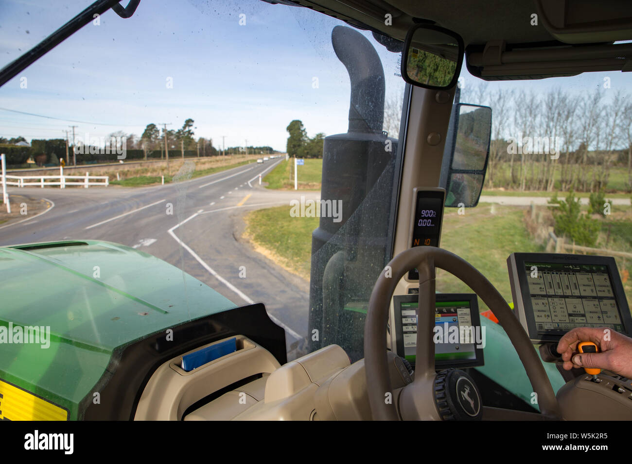 Sheffield, Canterbury, Nuova Zelanda, 27 Luglio 2019: un agricoltore aziona un grande e moderno di trattore John Deere per un campo di fattoria su strade di campagna Foto Stock