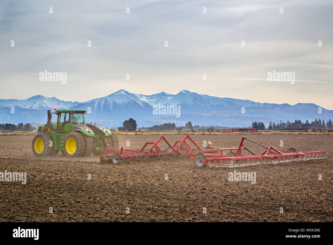 Sheffield, Canterbury, Nuova Zelanda, 27 Luglio 2019: un grande e moderno trattore John Deere rimorchia un coltivatore in un campo in inverno Foto Stock