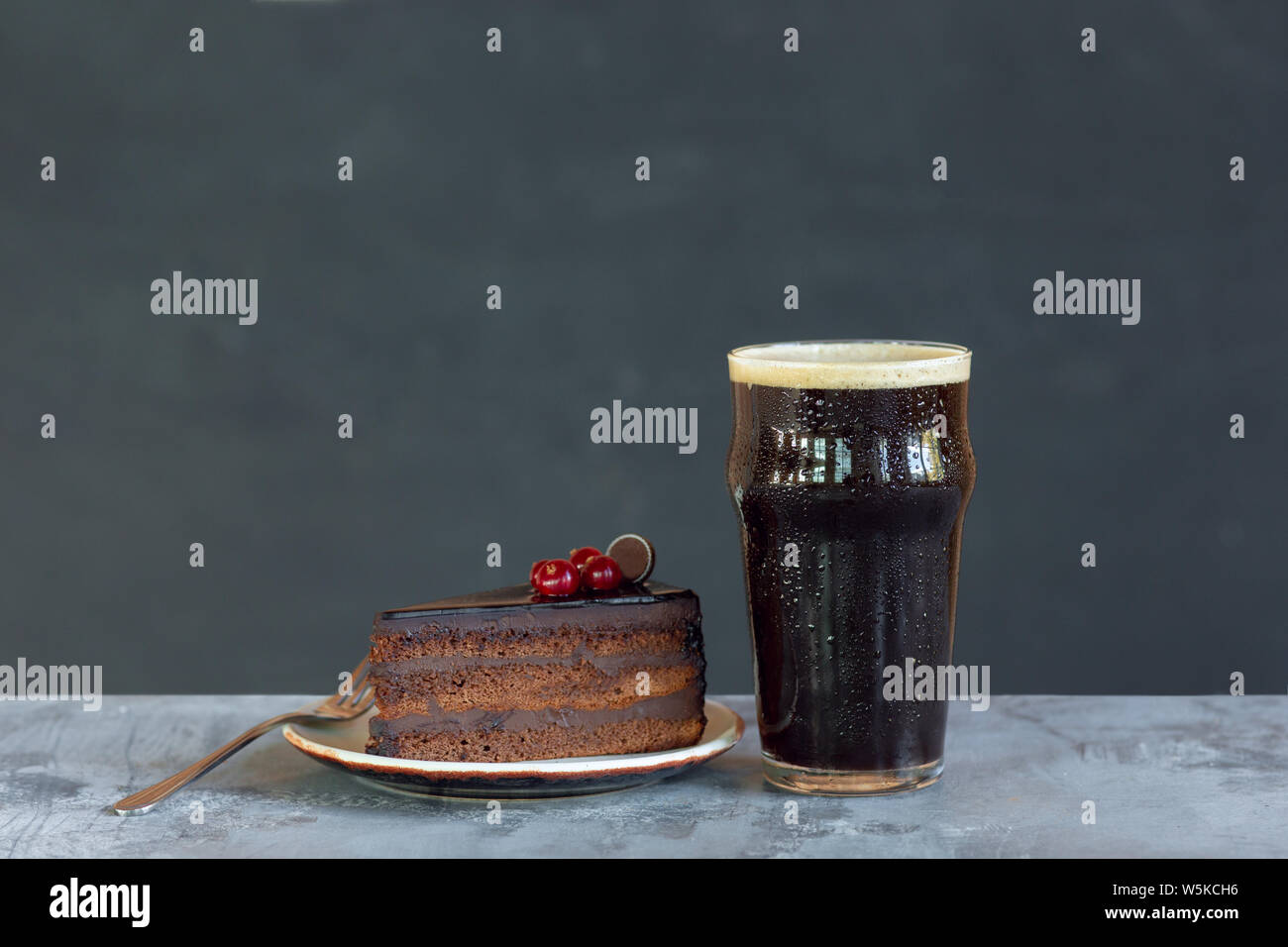 Bicchiere di birra scura sul tavolo di pietra e uno sfondo grigio. Bevanda fredda e tartufi con torta sono preparati per una grande festa. Concetto di bevande, divertente, cibo, celebrando, sale riunioni, Oktoberfest. Foto Stock