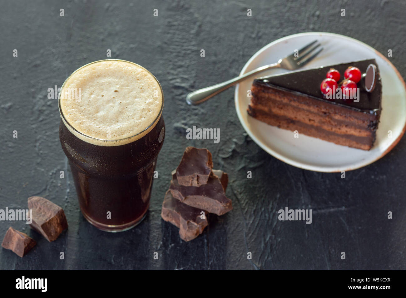 Bicchiere di birra scura sul tavolo di pietra dello sfondo. Bevanda fredda e tartufi con torta sono preparati per una grande festa. Concetto di bevande, divertente, cibo, celebrando, sale riunioni, Oktoberfest. Foto Stock