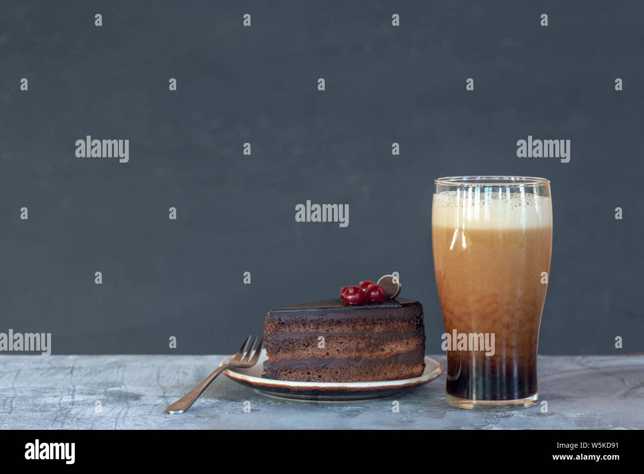 Bicchiere di birra scura sul tavolo di pietra e uno sfondo grigio. Bevanda fredda e una fetta di torta o dolci sono preparati per una grande festa. Concetto di bevande, divertente, cibo, celebrando, sale riunioni, Oktoberfest. Foto Stock