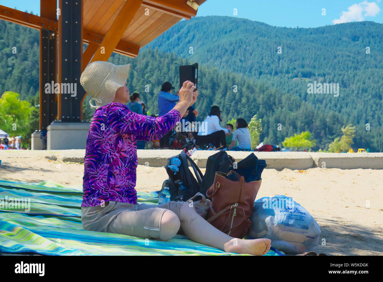 Una donna asiatica seduto su un telo da spiaggia mentre prendendo un selfie. Foto Stock
