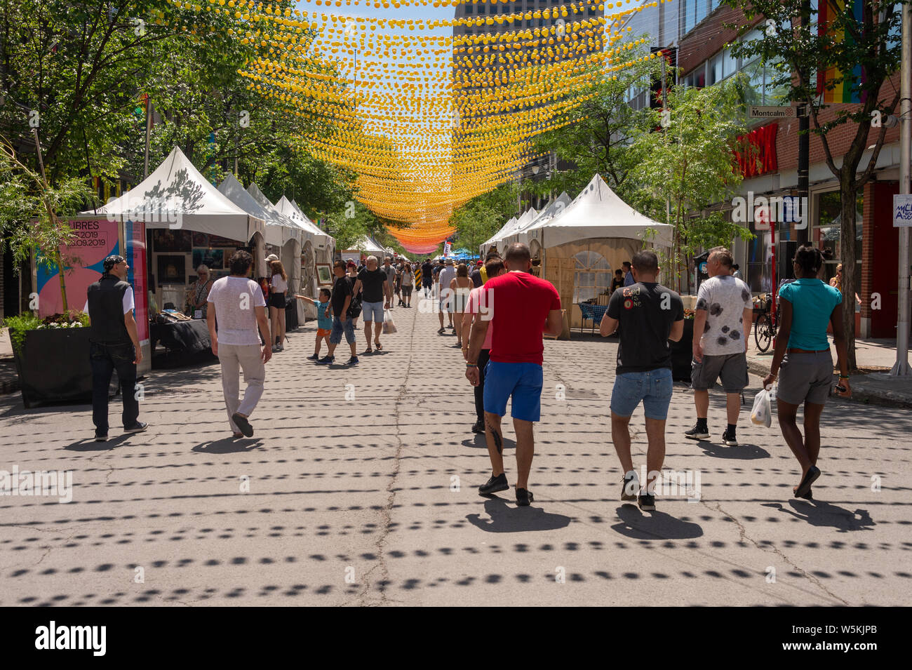 Montreal, CA - 1 Luglio 2019: la gente camminare al di sotto delle sfere di arcobaleno arte di installazione '18 tonalità di gay' su Saint-Catherine Street nel Villaggio Gay Foto Stock