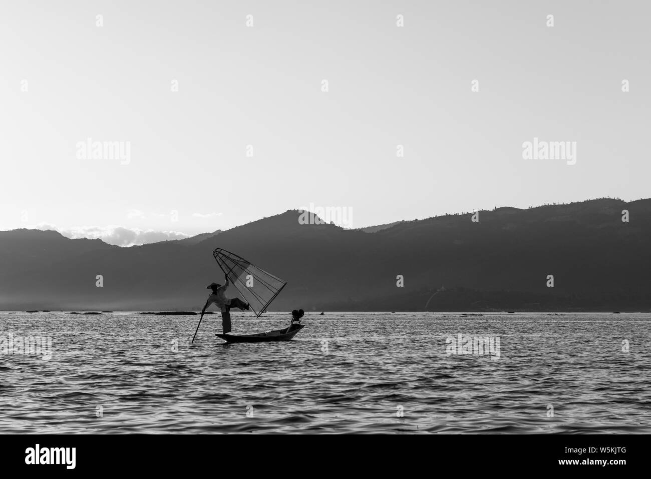 Immagine in bianco e nero di solitario pescatore birmano in possesso di una tradizionale rete a Lago Inle, Myanmar Foto Stock