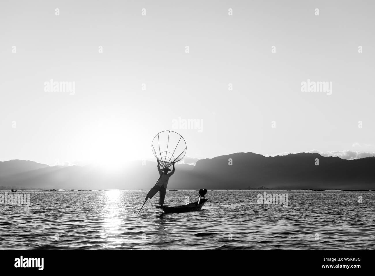 Immagine in bianco e nero del pescatore birmano silhouette tenendo una tradizionale rete a Lago Inle, Myanmar Foto Stock