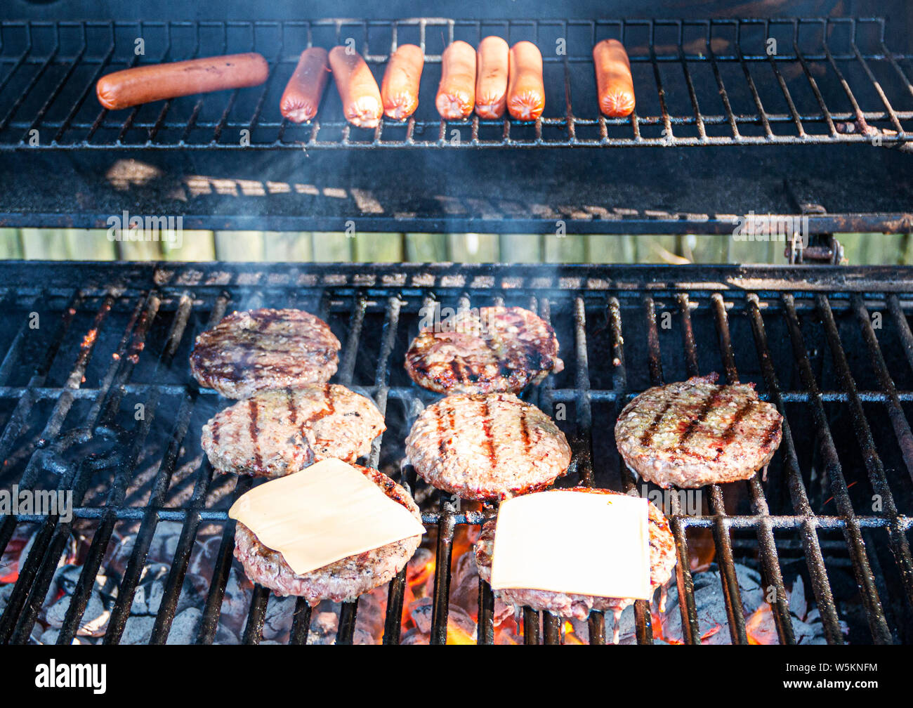 Hot Dog, Hamburger e cheeseburger sono in cottura su una graticola con carboni ardenti sotto. Foto Stock