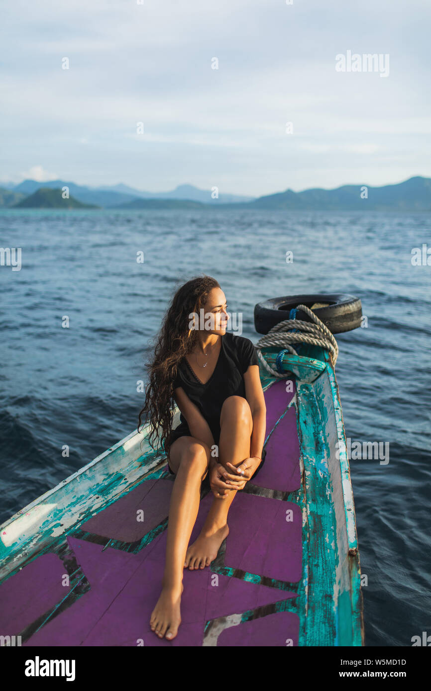 Giovane donna rilassante in barca al tramonto e guardando l'isola. Il vecchio tradizionale barca asiatici, viaggi in Indonesia Foto Stock