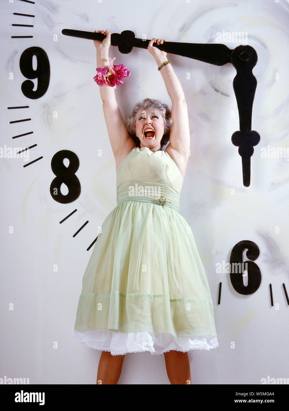 La donna in un abito di divertenti appesa da un gigantesco orologi Foto Stock