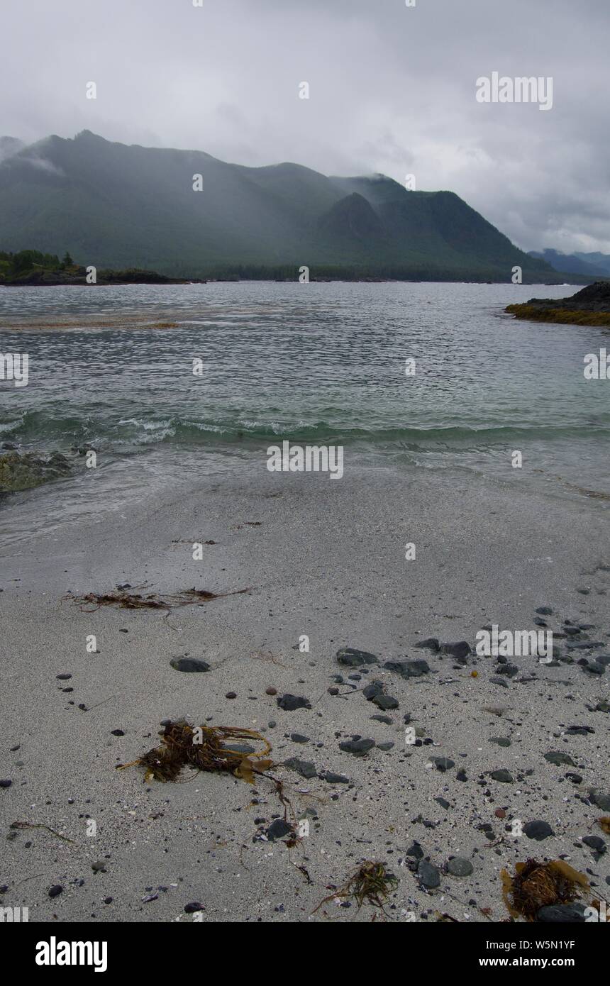 Le onde rompono sulla spiaggia come scroscio di pioggia colpisce le montagne in distanza, Nuchatlitz ingresso, British Columbia Foto Stock
