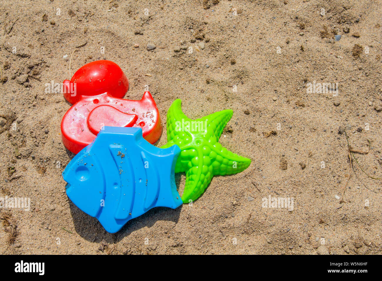 Giocattoli di sabbia sono fuori su una spiaggia di sabbia al sole: stampi di un rosso d'anatra, un pesce blu e una stella verde. Foto Stock