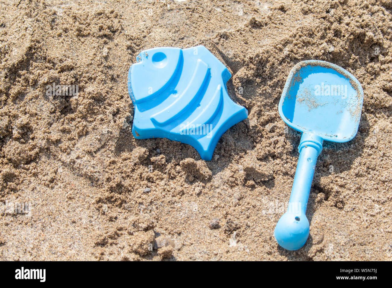 Blue Sand giocattoli, una pala e uno stampo di un pesce, sono distesi sulla sabbia su una spiaggia assolata in estate, in attesa di essere riprodotti con. Foto Stock