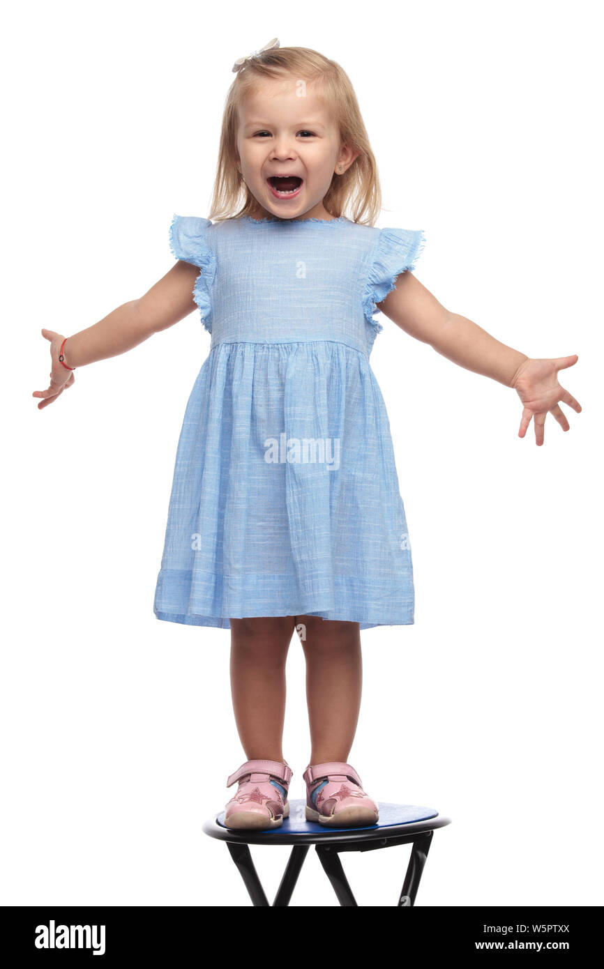 Super felice bambina in piedi su una sedia è accogliente con le braccia aperte su sfondo bianco Foto Stock
