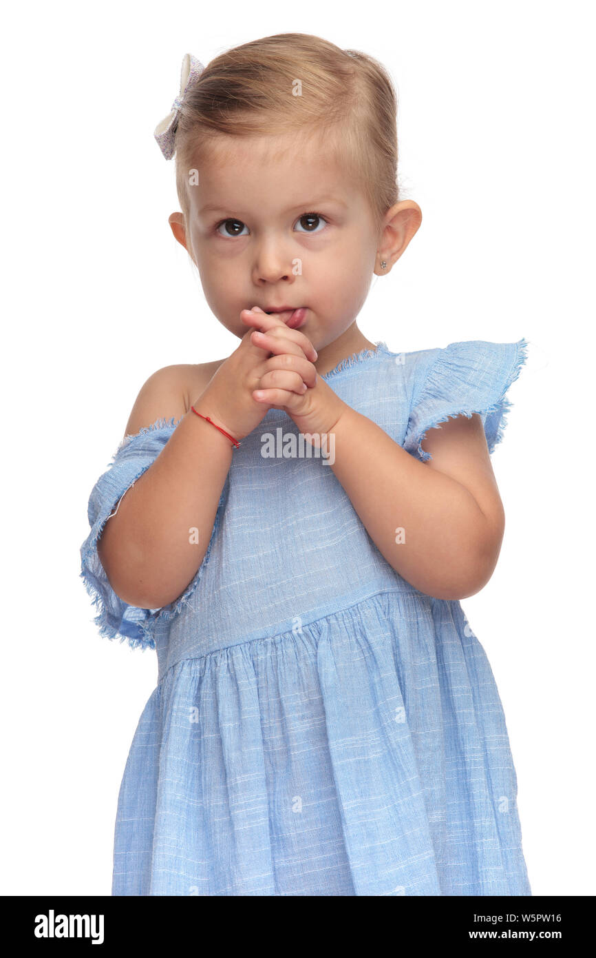 Carino bambina prega con palme insieme e un dito nella sua bocca su sfondo bianco Foto Stock