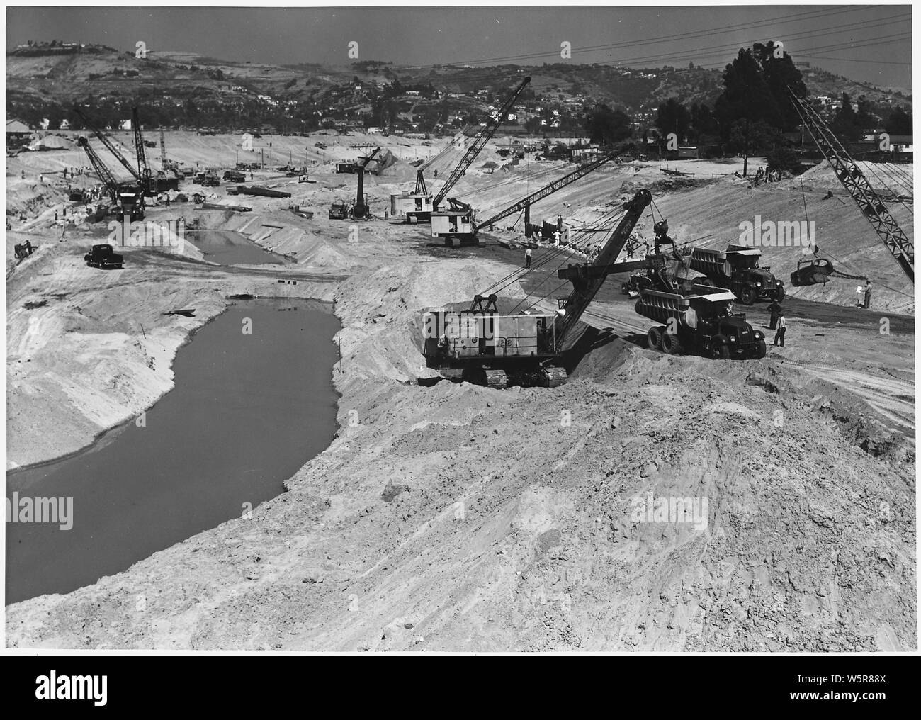 Los Angeles District - Fiume di Los Angeles Subproject No. 129 -' E.R.A. e regolari di fondi - lavoro noleggiato - preso in Giugno 13, 1938; l'ambito e il contenuto: Los Angeles District - Fiume di Los Angeles Subproject No. 129 -' E.R.A. e regolari di fondi - lavoro noleggiato - adottate il 13 giugno 1938. Vol. XI. No. 15. Questa vista del fiume di Los Angeles il canale è guardando a valle dalla Fletcher ponte di comando e mostra le varie fasi di costruzione del canale, compreso scavo in primo piano la guida in lamiera di acciaio Palancole dietro la trincea di punta nel centro superiore, l'immissione di Derrick pietra nella trincea di convergenza i Foto Stock