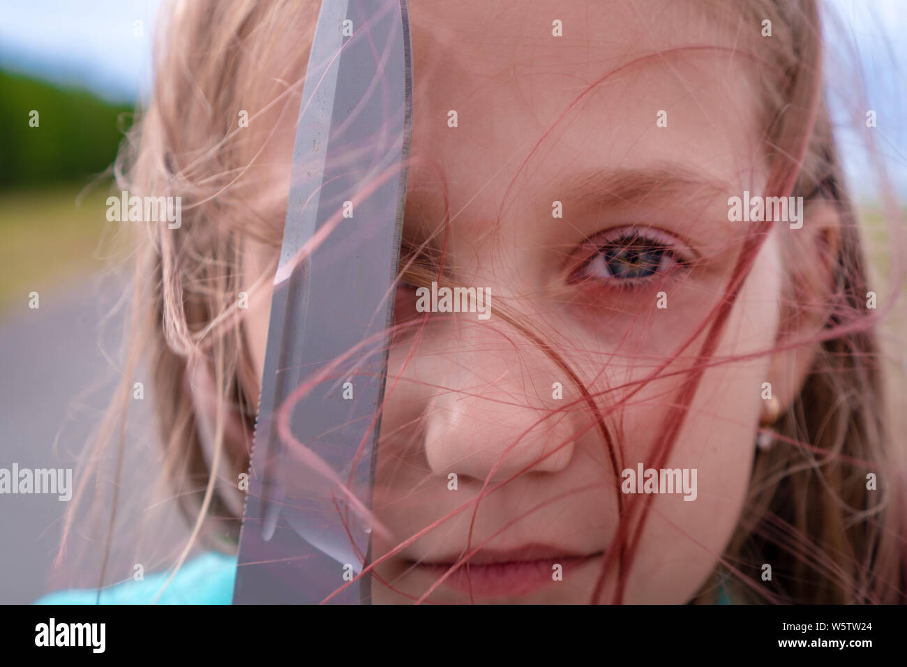 Ritratto di una bambina di 9 anni nelle sue mani con la lama di un coltello nella foresta. Un bambino sta guardando la telecamera e in possesso di un coltello nelle sue mani. Capelli rossi Foto Stock