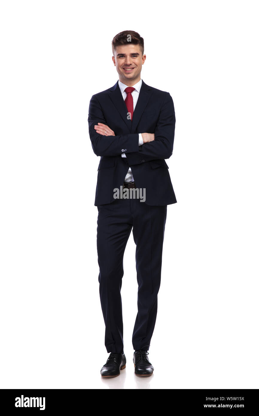 Happy businessman in piedi su sfondo bianco con le braccia incrociate, indossa una marina abito colorato e una cravatta rossa, corpo pieno foto Foto Stock