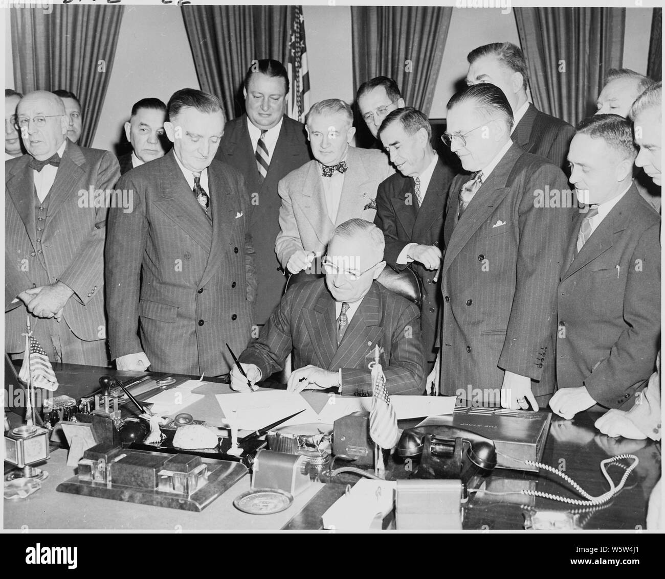 Fotografia del Presidente Truman alla sua scrivania in ufficio ovale, firma di S. 790, un atto di concessione del consenso degli Stati Uniti per la parte superiore del Fiume Colorado Basin compatto, come Segretario degli Interni Giulio Krug e membri delle delegazioni del congresso del Wyoming, dello Utah e Colorado, Nuovo Messico e Arizona a guardare. Foto Stock