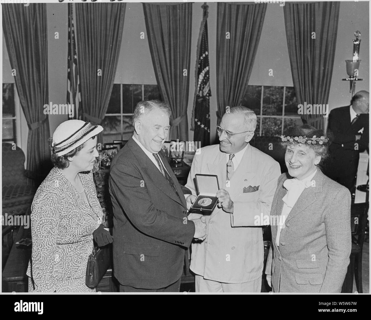 Fotografia del Presidente Truman all Ufficio Ovale, agitando le mani con il Vice Presidente Alben Barkley come egli lo presenta con una medaglia d'oro per servizio distinto nel Congresso, come Vice Presidente la moglie Jane Barkley (sinistra) e Nellie Tayloe Ross, direttore dell'Ufficio di presidenza della Zecca (a destra), a guardare. Foto Stock
