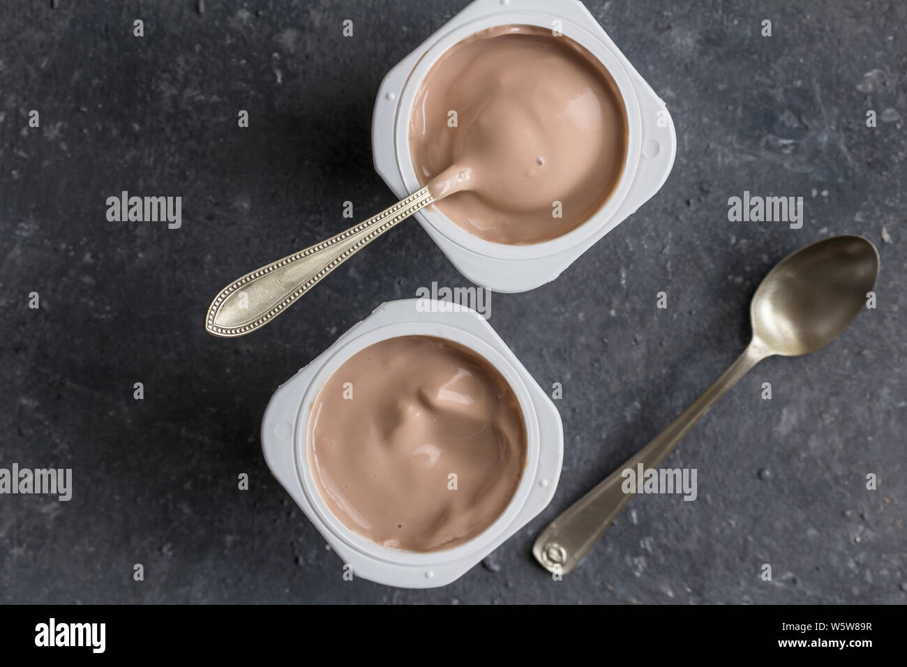 Due aromatizzato al cioccolato yogurt in bicchieri di plastica con cucchiai su grigio texture di sfondo - top view foto di tazze di yogurt Foto Stock