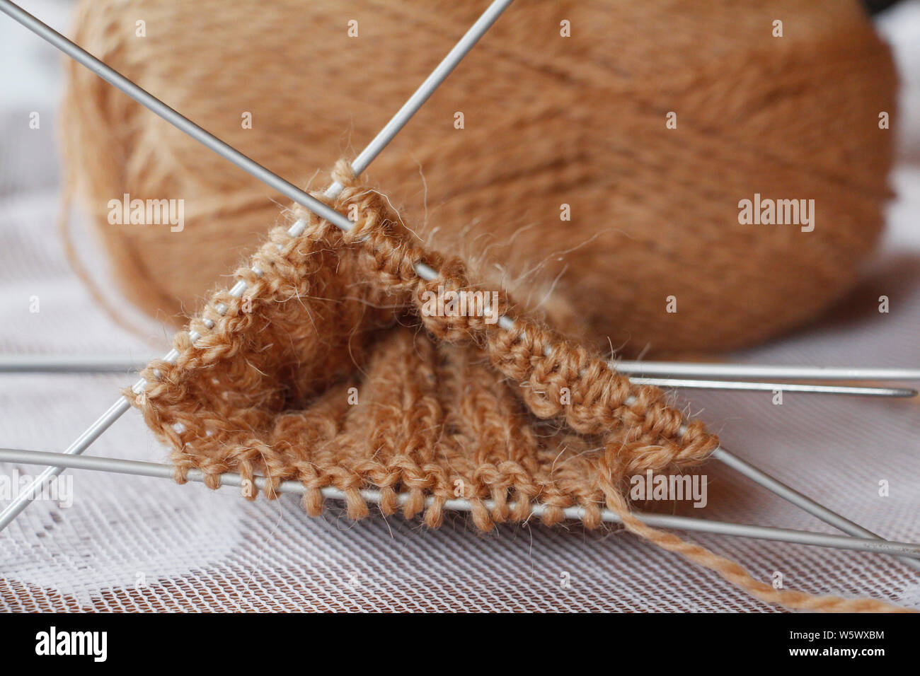 Matassa di filo e aghi da maglia. Lavorato a maglia. Ricamo. Maglia di lana per maglieria di punta. Il lavoro è iniziato. Colore marrone. Maglia guanti caldi con aghi. Foto Stock
