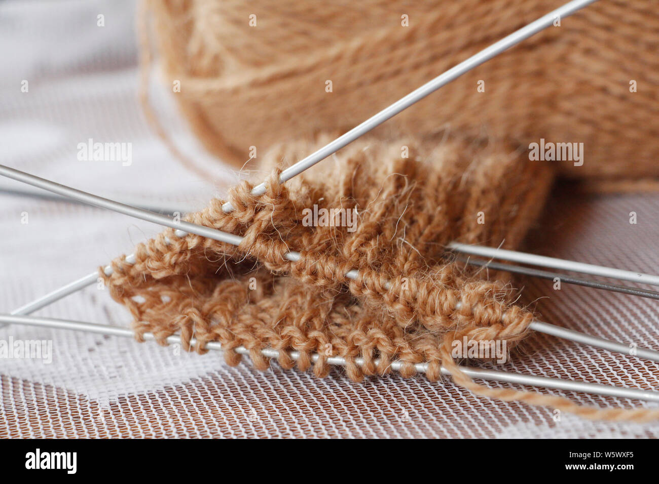 Matassa di filo e aghi da maglia. Lavorato a maglia. Ricamo. Maglia di lana per maglieria di punta. Il lavoro è iniziato. Colore marrone. Maglia guanti caldi con aghi. Foto Stock