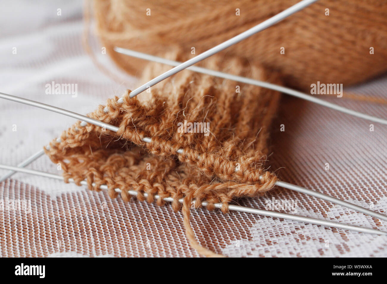 Matassa di filo e aghi da maglia. Lavorato a maglia. Ricamo. Maglia di lana per maglieria di punta. Il lavoro è iniziato. Colore marrone. Maglia guanti caldi con aghi. Foto Stock