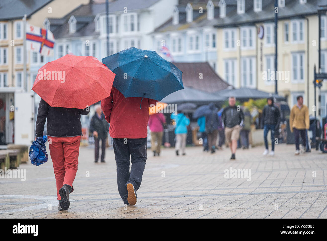 Aberystwyth, Wales, Regno Unito. Il 30 luglio 2019. I turisti nei loro impermeabili e ombrelli a piedi lungo la passeggiata in Aberystwyth sotto la pioggia come un nastro di thundery e umido molto tempo si diffonde attraverso molte delle parti centrali del Regno Unito, portando con sé il rischio di inondazione distruttiva e insidiose condizioni di guida. Credito Foto : Keith Morris/Alamy Live News Foto Stock
