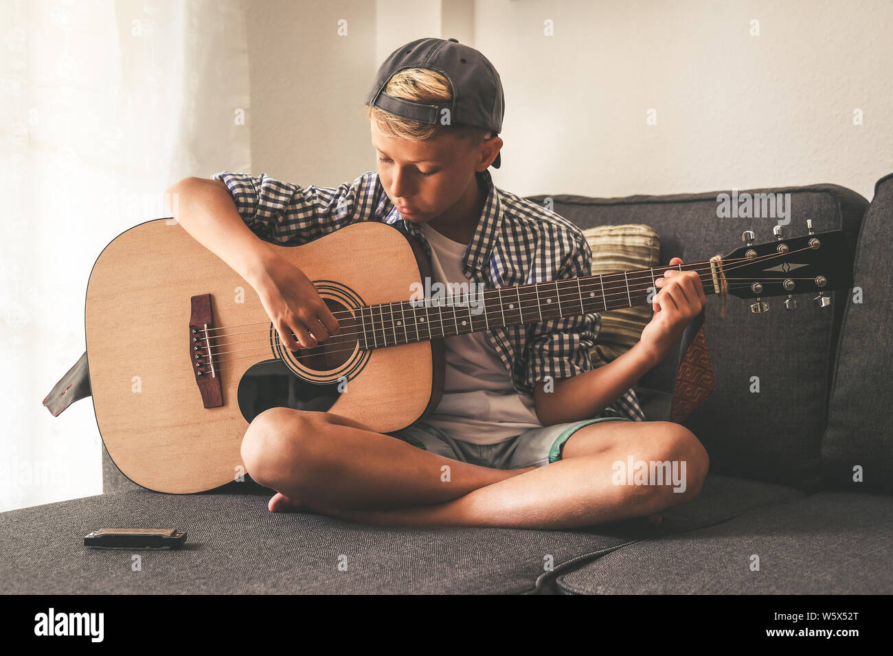Bella giovane ragazzo suonare la chitarra acustica. Studente di musica  esercizi a casa da solo. Alla moda bambino caucasico suona strumenti seduto  gambe incrociate su t Foto stock - Alamy