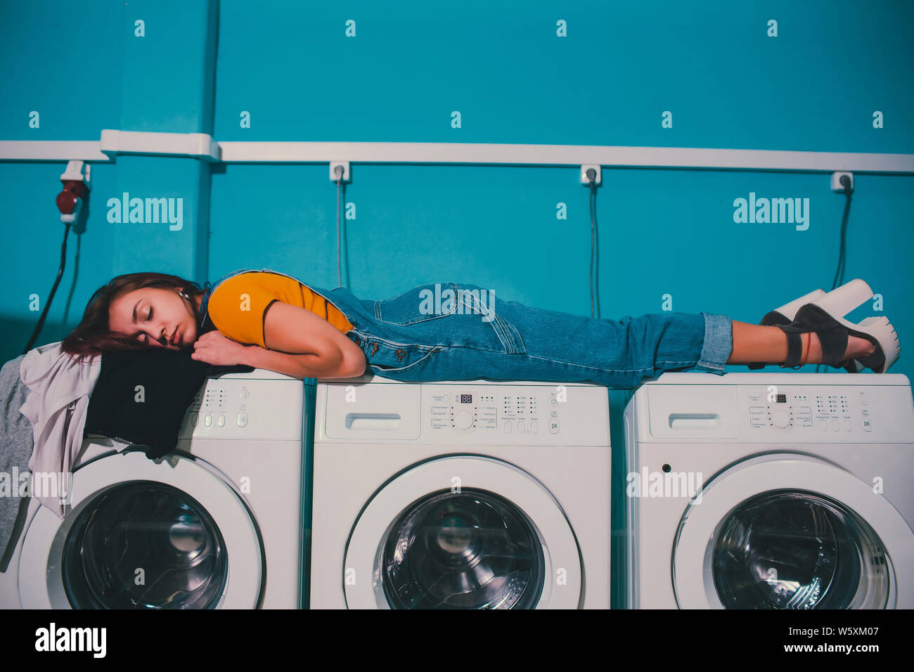 Giovane donna cercando vestiti nel cesto della macchina di lavaggio in lavatrici a gettone. Foto Stock
