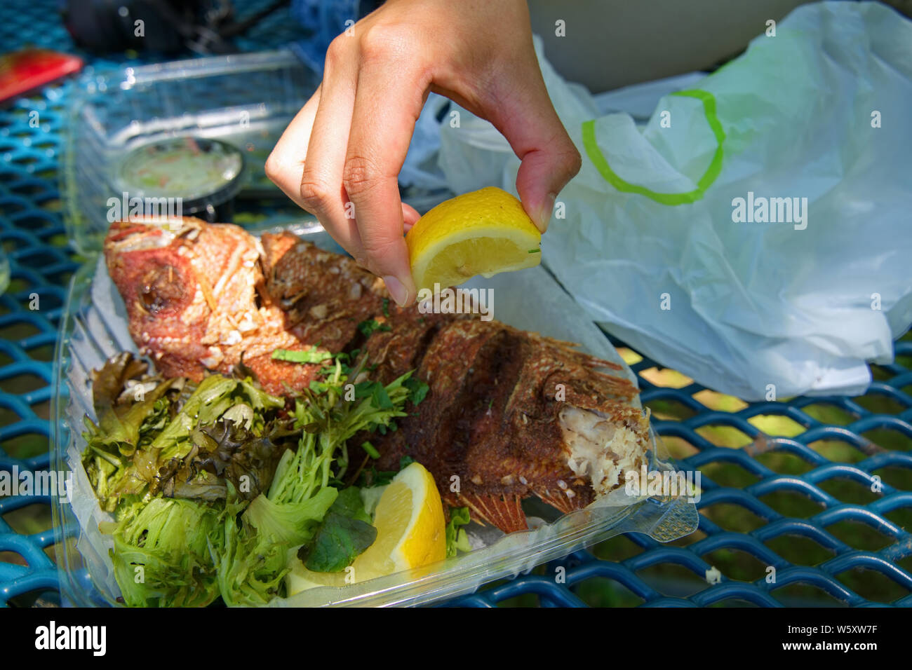 Spremitura a mano un taglio fresco limone su una succosa estrarre fried red snapper. Foto Stock