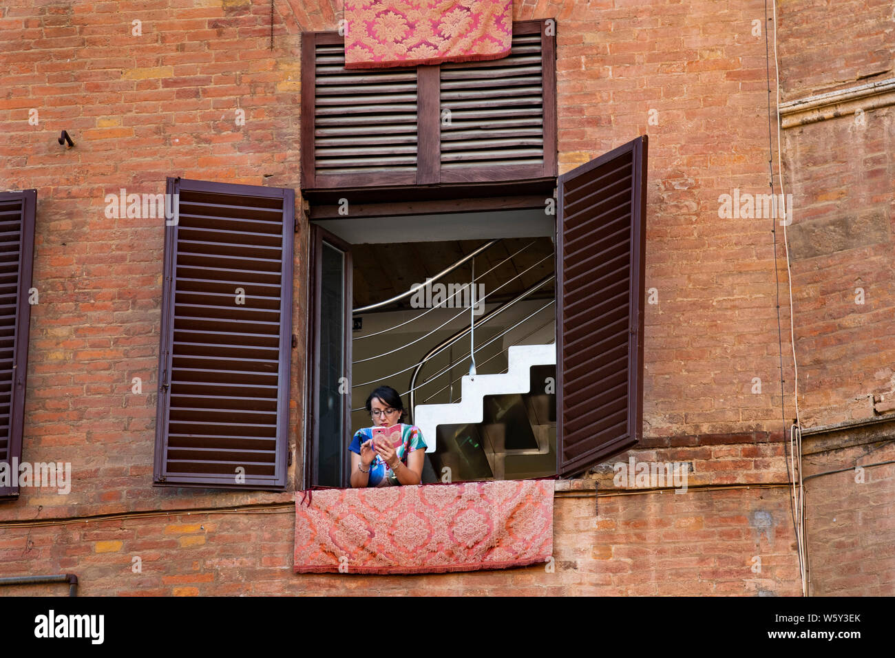 Dimentica gli eventi del Palio al di sotto di una donna nella finestra dei testi sul suo telefono cellulare in Siena, Italia Foto Stock