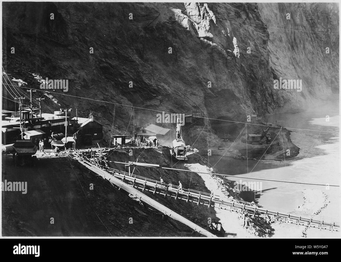 View all'uscita di portali di Nevada gallerie di diversione durante l'alluvione del 31 agosto 1932. Il raggiunge inferiore di tutti e quattro i tunnel di deviazione sono state inondate fino ad una profondità di 15' quando 58,000 c.f. versata attraverso Canyon Nero. Acque filtrate attraverso la terra e roccia barriere e lavato via le dighe di protezione. Nota la potenza di badili e di lavoro degli equipaggi per impedire ulteriori incursioni dell'acqua contro le arginature.; Portata e contenuto: fotografia dal volume due di una serie di album di foto per documentare la costruzione della Diga di Hoover, Boulder City, Nevada. Foto Stock