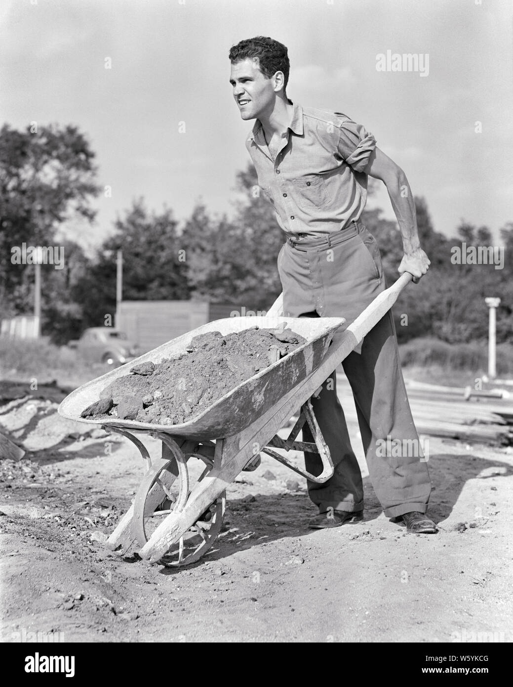 1940s giovane lavoratore edile operaio movimentazione carico di sporcizia con carriola - b11708 HAR001 HARS abilità Competenze occupazione resistenza carico esterno i progressi del lavoro di occupazioni utilizzando CONCETTUALE DEL LAVORO MANUALE noioso dura in bianco e nero di etnia caucasica HAR001 duro lavoro operaio in vecchio stile Foto Stock