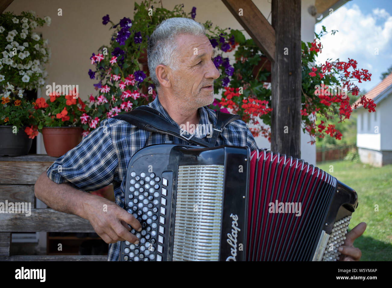 La Serbia, 20 Luglio 2019: Ritratto di un uomo locale giocando harmonica davanti a casa sua nel villaggio Solotuša Foto Stock