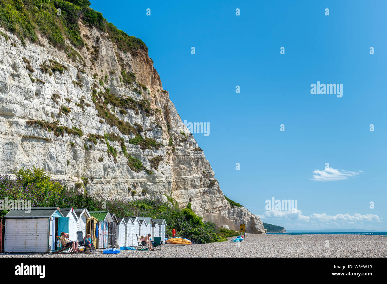 Birra, South East Devon, in Inghilterra. Vacanzieri godere il sole estivo accanto alle piccole baite che sedersi sotto le scogliere sulla spiaggia di birra in modo Foto Stock