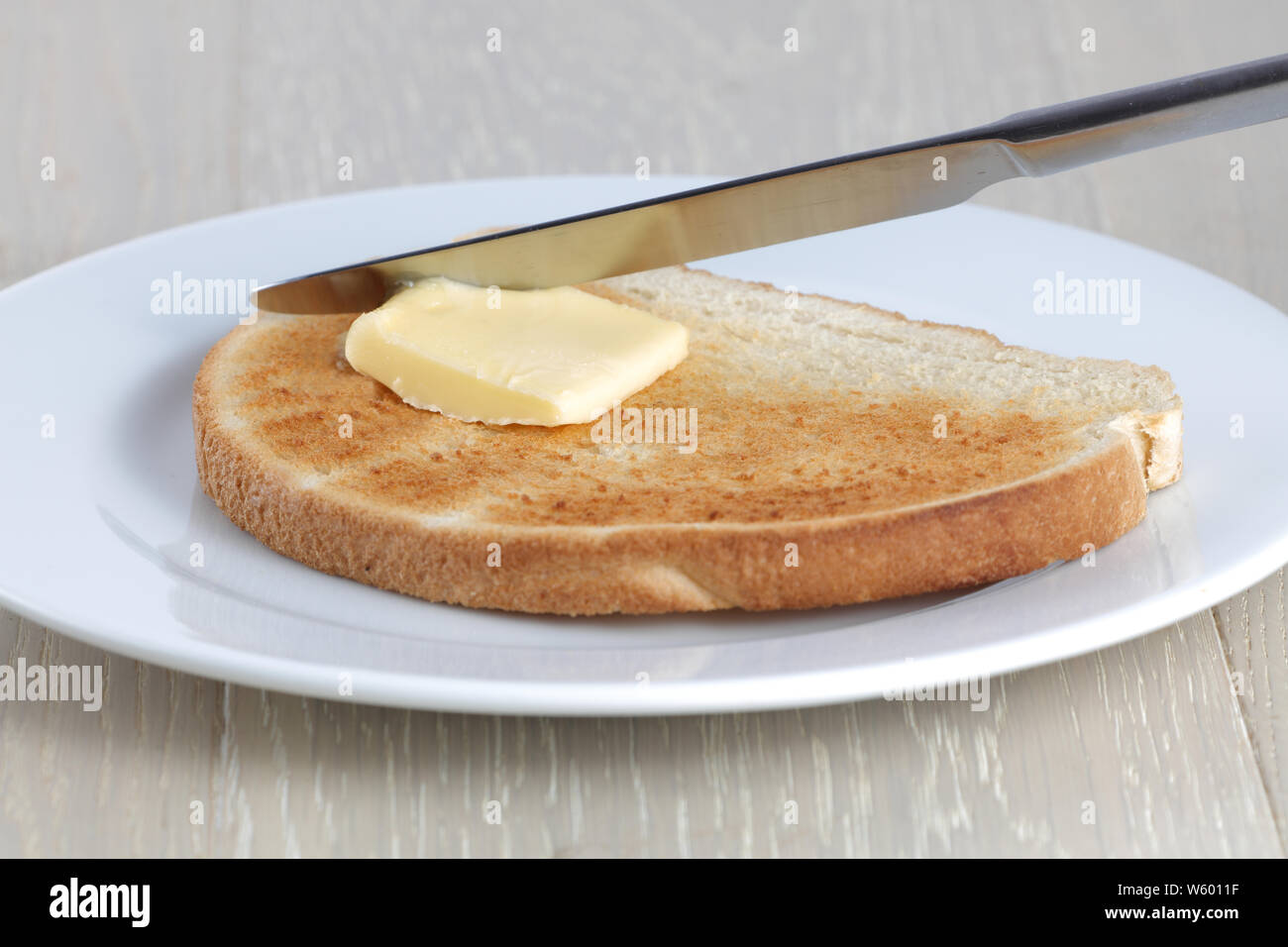 Una fetta di pane tostato e Coltello per burro su una piastra bianca Foto Stock