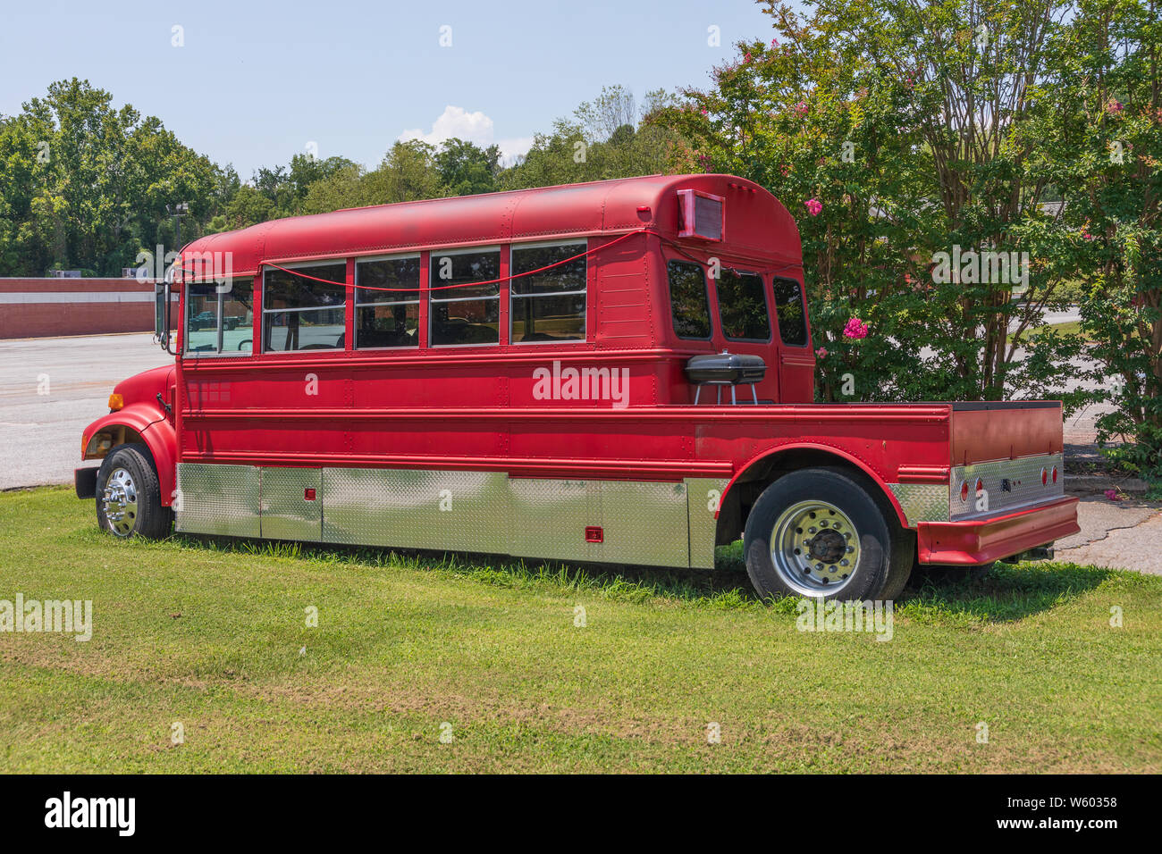 SPINDALE, NC, Stati Uniti d'America-27 luglio 19: un rosso scuola convertito convertito in un camper con un 'veranda sul retro' e grill, imposta in un prato molto su un giorno d'estate. Foto Stock