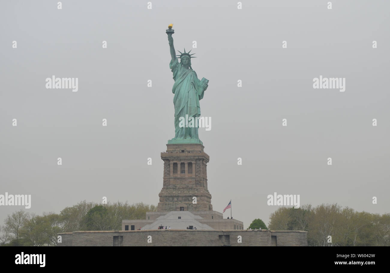 Primavera a New York City: Statua della libertà (bandiera americana a destra) in una mattinata Overcast Foto Stock
