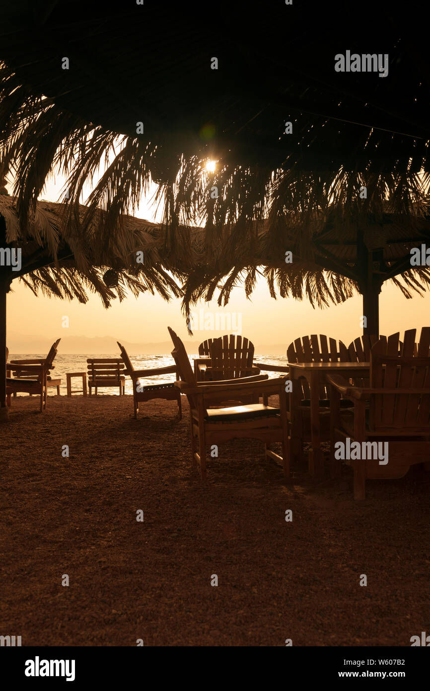 A Dahab, sul Sinai egiziana, un ristorante sulla spiaggia vi aspetta patroni. Il Golden Sun si innalza al di sopra della Saudi Arabian coast attraverso il golfo di Aqaba. Foto Stock