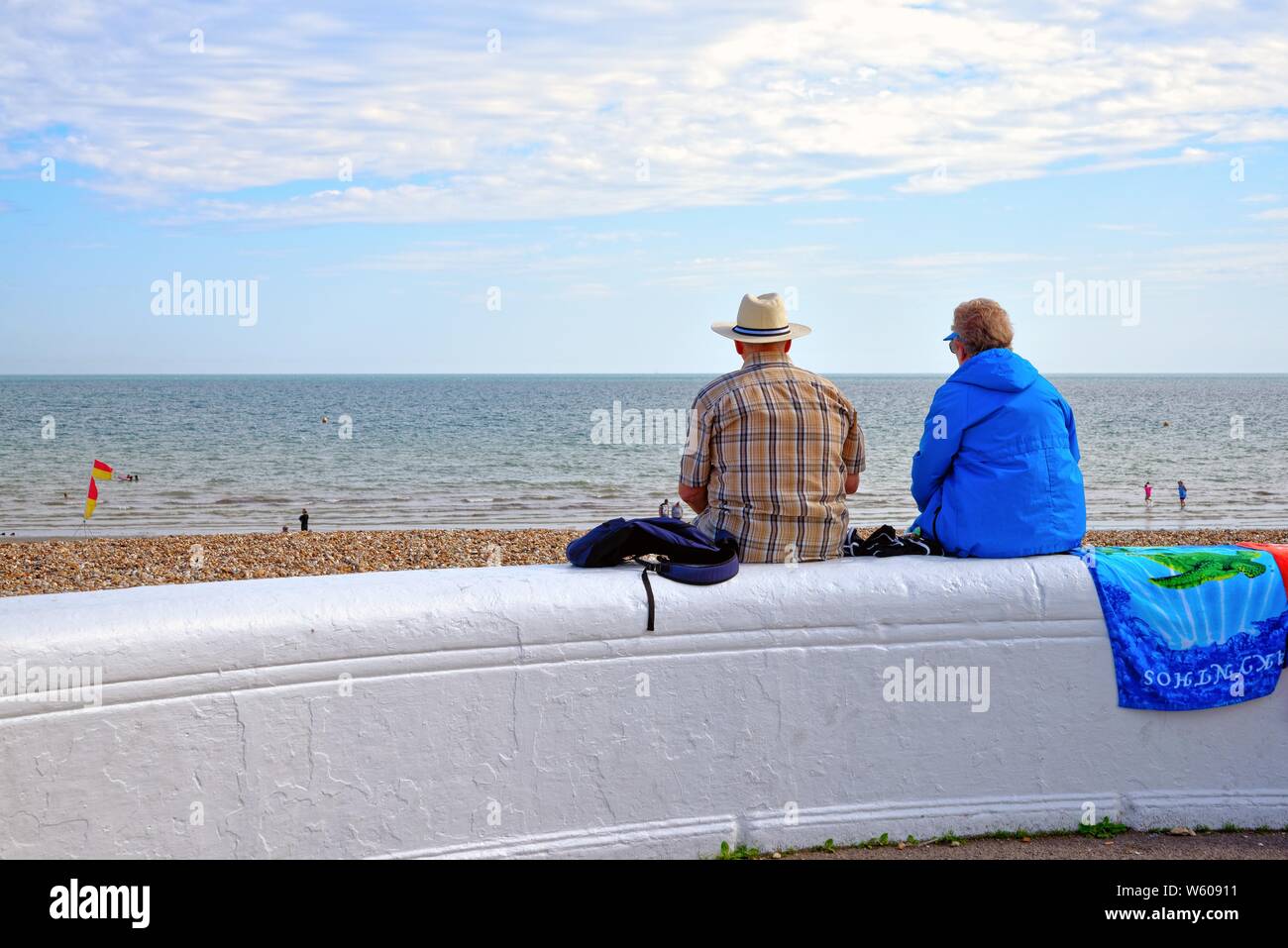 Vista posteriore di una coppia di anziani seduti su un muro sul lungomare che si affaccia sul mare da una giornata d'estate, Bognor West Sussex England Regno Unito Foto Stock