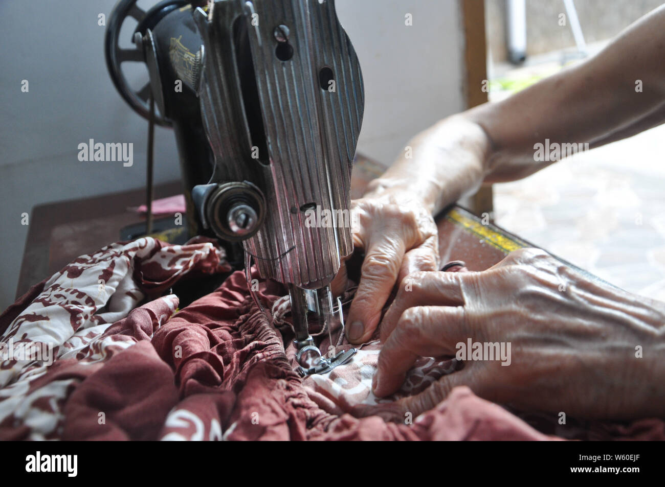 Dortje Nony, 73, cuce un panno in casa sua. Mrs.Nony si prende cura del suo marito Andarias Sarra, 80, una corsa vittima che sopravvivere da due attacchi di corsa Foto Stock
