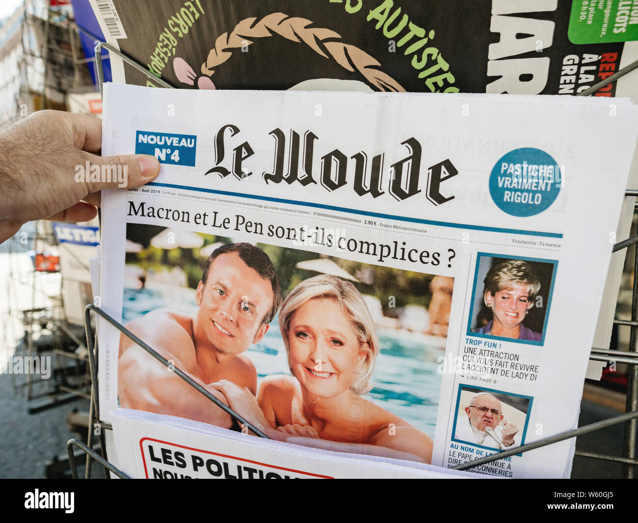 Parigi, Francia - Lug 24, 2019: Man mano che tiene il satirico Le Woude quotidiano a French press kiosk con collage del presidente francese Emmanuel Macron e Marine Le Pen Foto Stock
