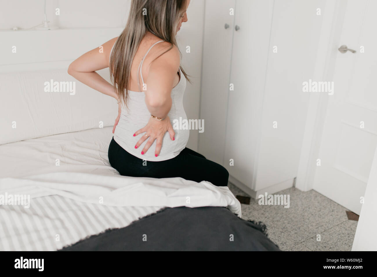 Donna incinta seduta sul bordo del letto con un mal di schiena Foto Stock