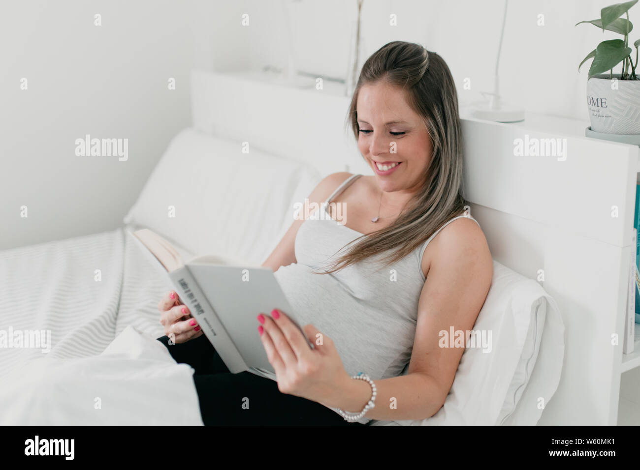 Incinta donna bionda che giace nel letto la lettura di un libro Foto Stock