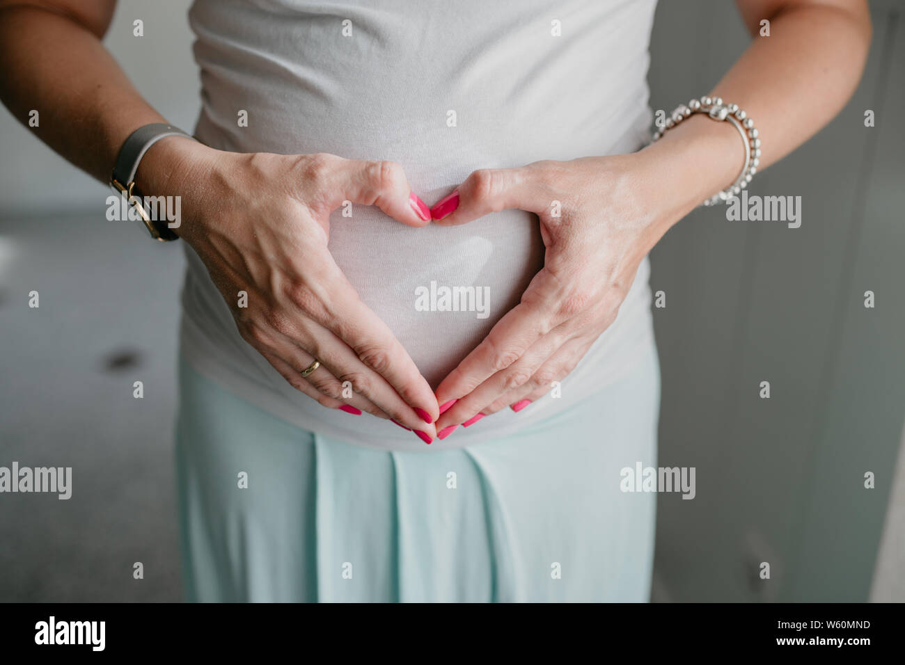 Donna incinta fa un cuore con le mani sul suo ventre Foto Stock