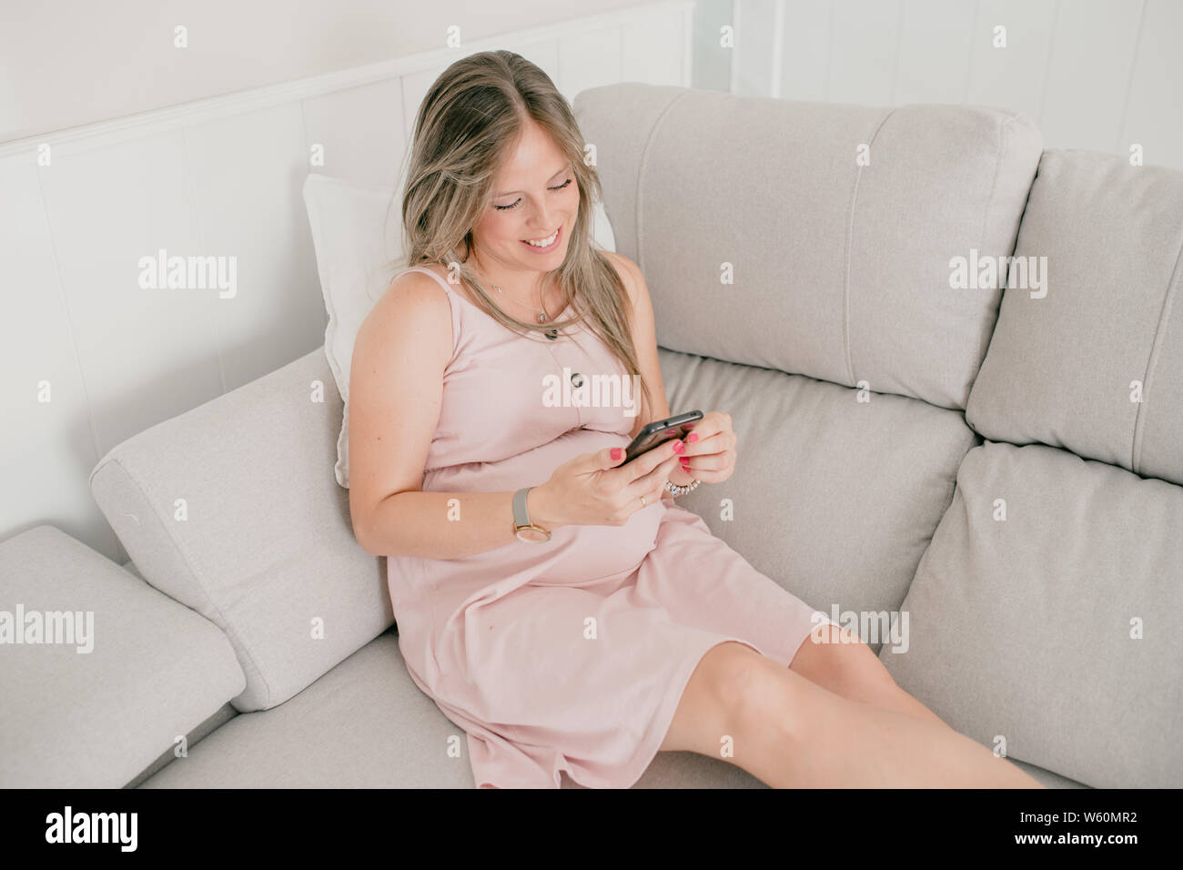 Felice donna incinta seduti in un divano guardando al telefono cellulare Foto Stock