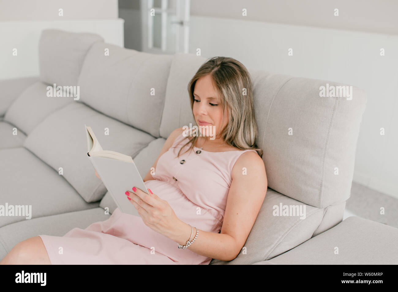 White donna incinta per leggere un libro nel divano del soggiorno Foto Stock