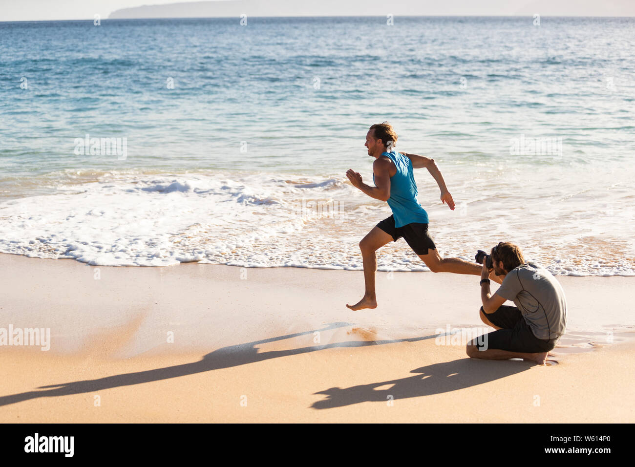 Dietro le quinte del servizio fotografico di maschio sport atleta modello funzionante per il fotografo a scattare foto per sport photoshoot. BTS sulla spiaggia. Foto Stock